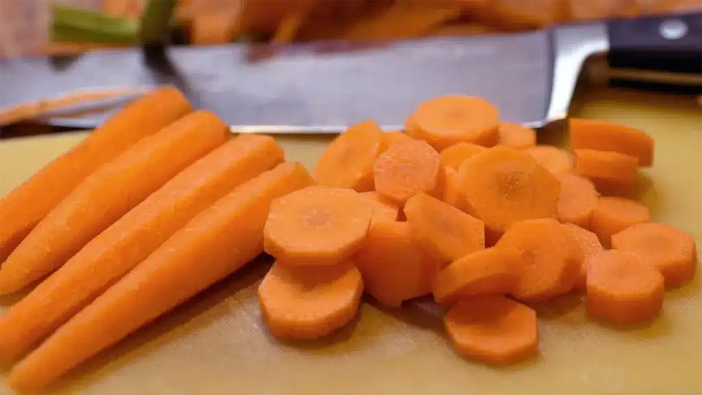 Peeled whole carrots and sliced carrot pieces next to a kitchen tool on a cutting board